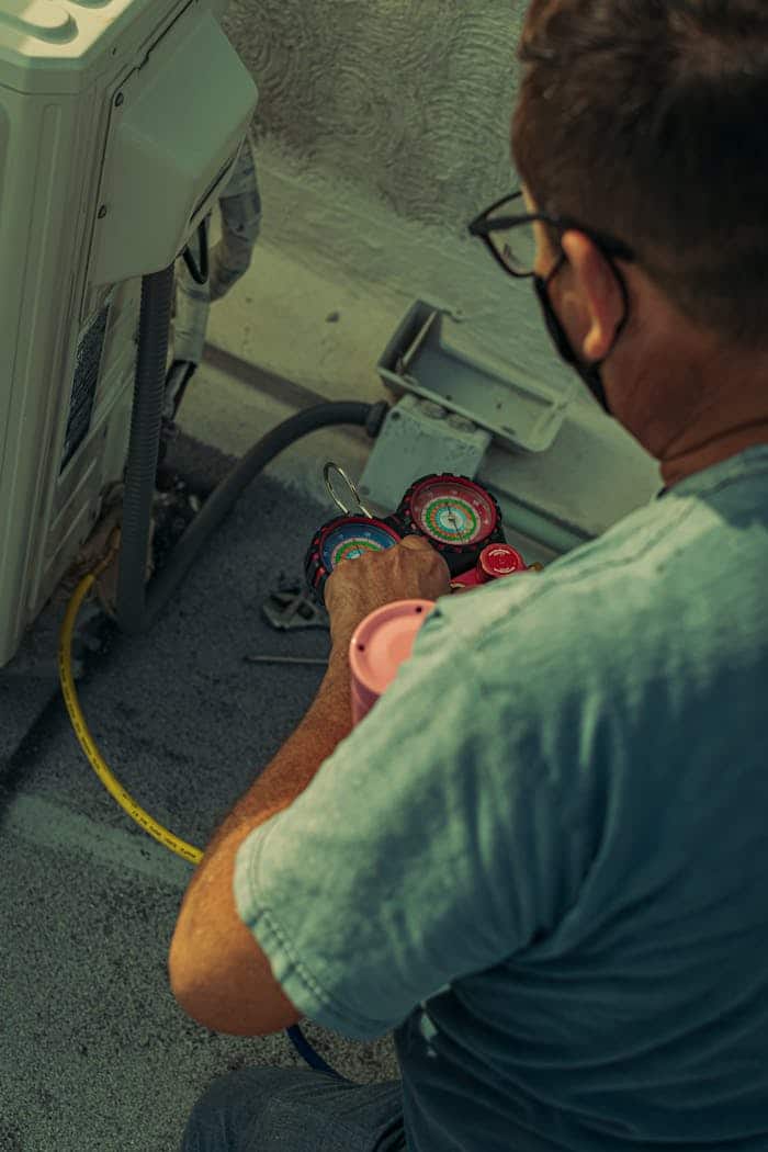 Professional technician repairing an outdoor air conditioning unit with gauges and tools.